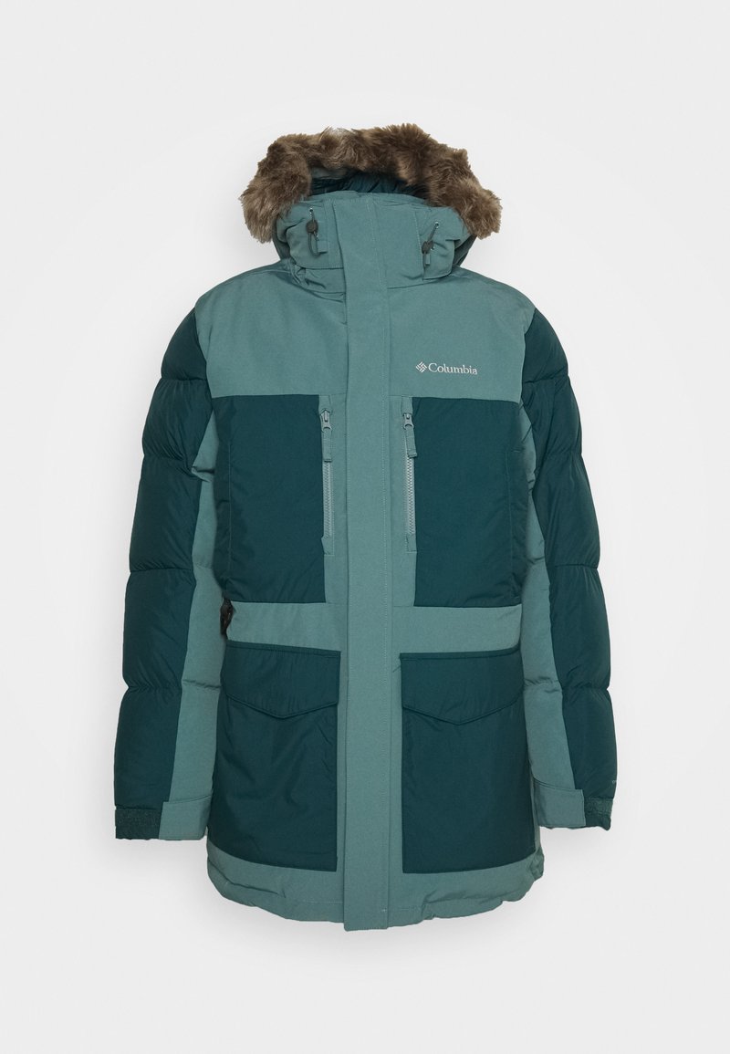 Veste en duvet verte avec capuche en fourrure, arborant des blocs de couleur contrastés, deux poches poitrine zippées et des poignets élastiques pour plus de chaleur.
