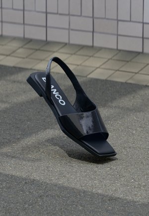 Črni sandali z naramnicami iz patentiranega usnja s kvadratnim prstom in minimalističnim oblikovanjem trakov. Imajo raven podplat in izrazito blagovno znamko.