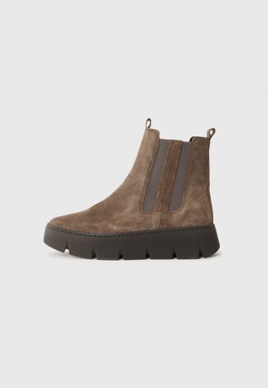 Bottines en suede marron avec panneaux élastiques sur les côtés, bout rond et épaisse semelle en caoutchouc noir. Équipées de languettes pour un enfilage facile.