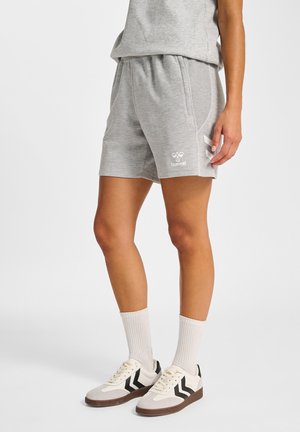 Osoba ubrana w jasnoszare spodenki hummel i pasujący top, białe skarpetki oraz białe trampki z czarnymi wzorami w kształcie szewrona.