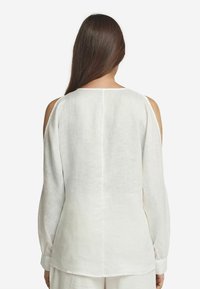 Blusa bianca di lino con maniche lunghe e ampia svasatura, e design con spalle scoperte. Presenta un collo rotondo e una cucitura dritta sul retro.