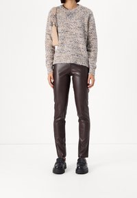 Beige gestrickter Pullover mit mehrfarbigen Sprenkeln, kombiniert mit braunen Lederhosen. Schwarze klobige Loafer vervollständigen das Outfit.