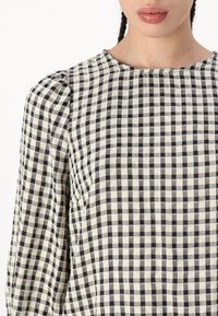 Top a scacchi neri e crema con scollatura arrotondata e maniche a sbuffo, realizzato in un tessuto con un aspetto texturizzato e intrecciato.