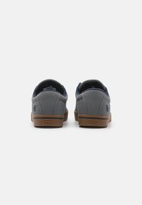 Adidași gri din pânză cu accente albastre închise, design de profil scăzut, guler căptușit și talpă din cauciuc maro. Prezentă logo pe călcâi.