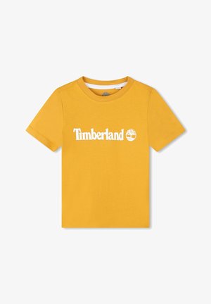 Camiseta de algodón amarilla con mangas cortas y cuello redondo. Presenta un logotipo blanco de "Timberland" y un emblema de árbol en la parte frontal.