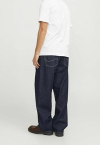 Mörkblå denimjeans med lös passform, med kontrasterande sömmar och två bakfickor, kombinerat med en enkel vit t-shirt.