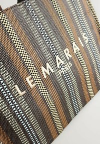 Woven tote bag featuring vertical stripes in brown, beige, light blue, and black with the embossed text "LE MARAIS PARIS" in cream.