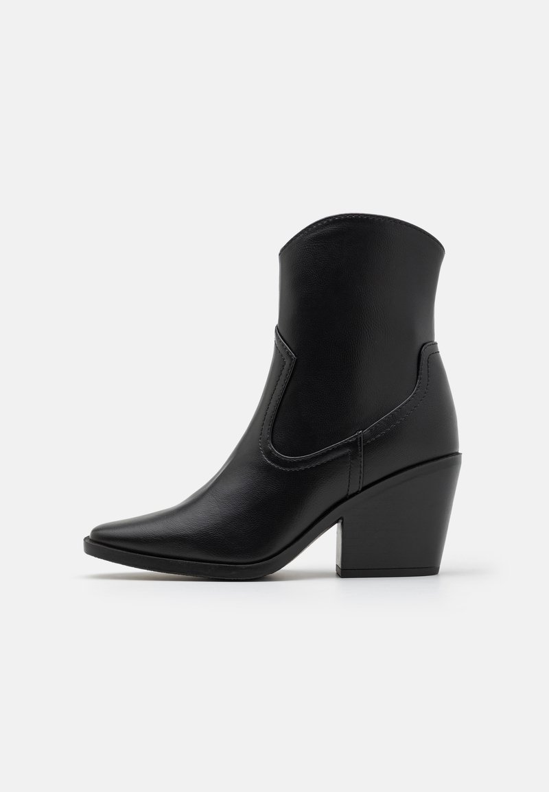 Botte western en cuir noir mi-mollet, bout pointu et talon bloc épais, sur un fond clair uni.