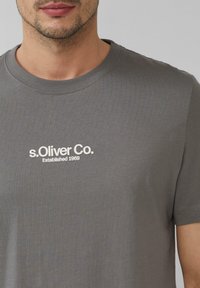 Grijze katoenen T-shirt met korte mouwen, voorzien van een ronde halslijn en een witte bedrukte logo "s.Oliver Co. Established 1969" op de borst.