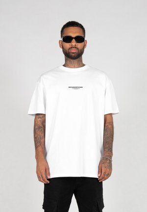 White cotton t-shirt with short sleeves and a round neck, featuring a small black printed text logo on the chest.