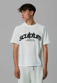 Hvid bomulds T-shirt med en stor sort grafisk tekst "sculpture" og mindre tekst "COLLECTIVE APPAREL EDITION," med korte ærmer.