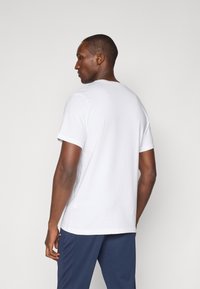 Hvid bomulds T-shirt med rund halsudskæring, korte ærmer og en løs pasform. Synlige sømme og en glat tekstur. Kombineret med marineblå bukser.