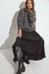 Suéter gris de punto con mangas oversized, combinado con una falda larga de satén negra y botas de cuero negras hasta la rodilla. Look simple y sofisticado.
