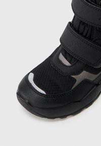 Czarne buty sportowe z teksturowaną cholewką z tkaniny, odblaskowymi akcentami i podwójnymi zapięciami na rzep. Wytrzymała gumowa podeszwa zapewniająca lepszą przyczepność.