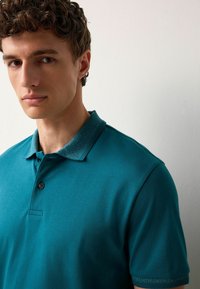 Türkiz polo póló, texturált gallérral és ujjakkal, egysoros gombos nyakkal, sima anyagból készült, slim fit kivitelben.
