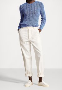 Blå kabelstickad tröja i kombination med vita, uppvikta byxor och vita sneakers. Tröjan har rund hals och strukturerat mönster.