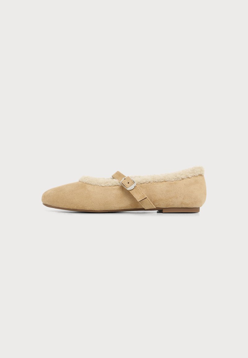 Chaussure plate beige avec une doublure en fourrure douce, un bout arrondi et une bride réglable avec une boucle argentée sur le côté.