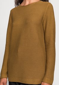 Sweter z długim rękawem wykonany z fakturowanej ribbed dzianiny w ciepłym odcieniu musztardowym. Posiada okrągły dekolt i prosty krój.