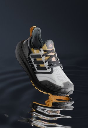 Hardloopschoen met zwart, wit en geel ontwerp zwevend boven reflecterend donker water met zichtbaar Adidas-logo en Gore-Tex-label.