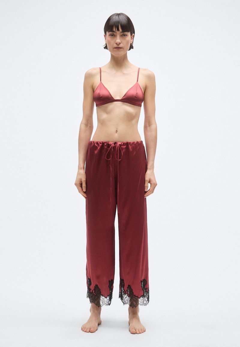 Czerwona satynowa braletka z cienkimi ramiączkami oraz pasujące czerwone satynowe spodnie z czarną koronkową lamówką na dole, o luźnym kroju i ściągaczu w pasie.