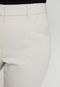 Vaaleanharmaat housut, joissa on sileä pinta, litteä etuosa, sivutaskut ja normaali vyöt ärö, jossa on vyölenkit.