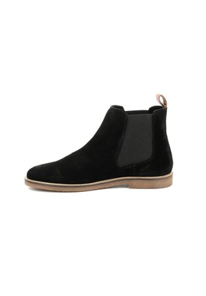 Bota chelsea de ante negra con paneles laterales elásticos, punta redondeada y un pequeño tacón marrón claro. Presenta una lengüeta en la parte posterior para facilitar su uso.