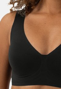 Zwarte draadloze bh met een brede band, diepe V-halslijn en een gladde stofstructuur, ontworpen voor comfort en ondersteuning.