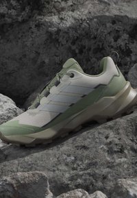 Chaussure de course extérieure verte et beige avec une semelle texturée reposant sur une surface rocheuse rugueuse.