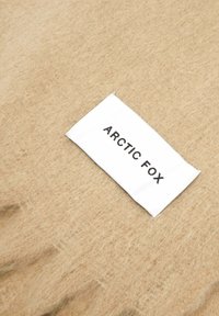 Tissu en feutre beige avec une étiquette blanche portant l'inscription "ARCTIC FOX" en texte noir. La texture semble douce et duveteuse, avec une surface lisse.