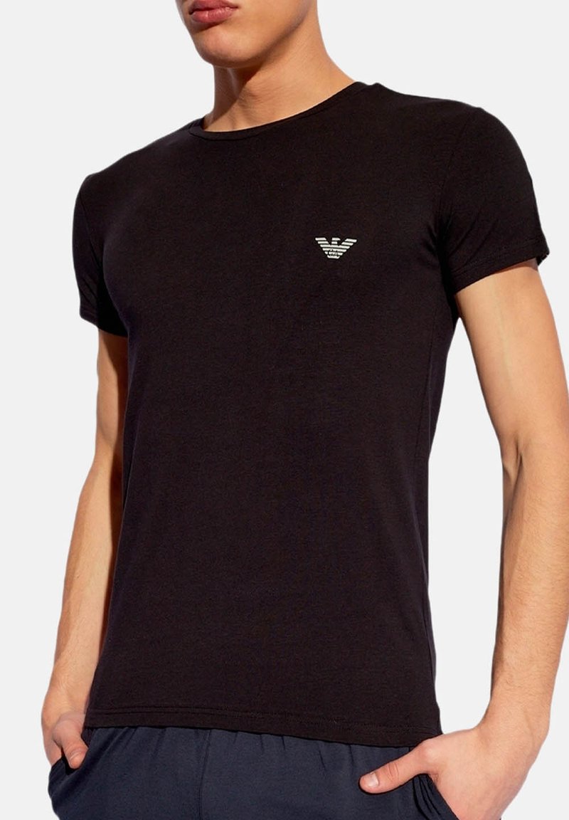 T-shirt noir à manches courtes en coton. Présente un petit logo imprimé sur la poitrine. Design simple et ajusté avec un col rond.
