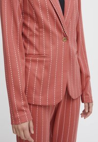 Rust-colored blazer with white vertical pinstripes, single front button, notch lapel, and a side pocket. Smooth fabric texture.