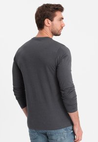 Grå långärmad skjorta i mjukt bomullsmaterial, med rund halsringning och åtsittande ärmslut, kombinerad med ljusblå jeans.