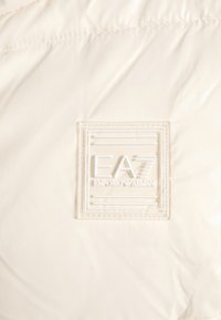 Tessuto bianco con una chiara toppa quadrata considerata con il logo "EA7 Emporio Armani" in lettere e linee in rilievo.