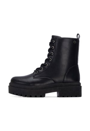 Botas de cuero negro hasta el tobillo con cordones en la parte delantera, suela de goma gruesa y ojetes metálicos; incluye una tira en la parte trasera para facilitar el calzado.