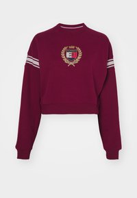 Sudadera cortada en burdeos hecha de tela suave, con un parche de logo, acentos de franjas blancas en las mangas y un cuello redondo.