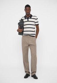 Prugasta polo majica u krem i tamnoplavoj boji, uparena s smešnim smešnim hlačama i crnim cipelama. Model drži crnu kožnu jaknu.