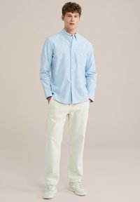 Lichtblauw button-up overhemd met lange mouwen, borstzak, gecombineerd met witte relaxte broek en witte sneakers. Gladde stofstructuur.