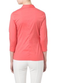 Blusa coral de manga tres cuartos con cuello, textura suave y detalle de costura trasera, llevada sobre pantalones blancos.
