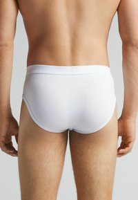 Weiße Baumwollslips mit einfach gehaltenem Design, elastischem Bund und glatter Textur, die einen eng anliegenden Schnitt hinten zeigen.