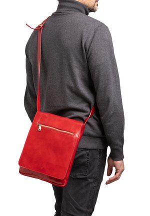 Homme portant un pull gris foncé et un jean avec un sac bandoulière en cuir rouge vif, doté d'une poche zippée à l'avant, porté sur l'épaule.