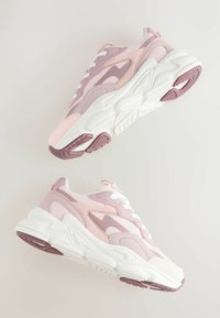 Adidași roz și lavandă cu un design textil stratificat, talpă albă și talpă exterioară din cauciuc texturat. Șireturile sunt albe cu accente corespunzătoare.