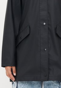 Black waterproof jacket with a button-front closure, side pockets, and a smooth texture. Visible stitching along the hem and sleeves.