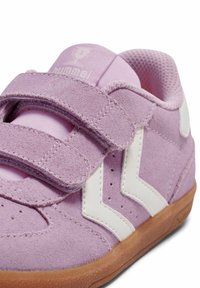 Fioletowy zamszowy sneaker z białymi akcentami, wyposażony w podwójne rzepy i podeszwę z gumy w kolorze karmelowym. Posiada perforacje na cholewce.