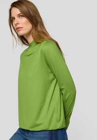 Grünes Langarmoberteil mit hohem Ausschnitt und lockerer Passform. Hergestellt aus glattem Stoff, mit gerafften Details am Saum und an den Bündchen.