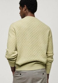 Lichtgele, gestructureerde trui met een ruitpatroon, ronde hals en ribgebreide manchetten. Draag met lichtgrijze broek met twee achterzakken.