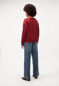 Felpa bordeaux con vestibilità comoda e scollatura a girocollo, abbinata a jeans a gamba larga blu chiaro. Tessuto morbido e dettagli minimi.