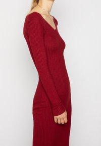 Robe à manches longues côtelée d'un rouge profond, avec un décolleté en V et une silhouette ajustée. Texture douce avec un léger stretch, conçue pour un look épuré.
