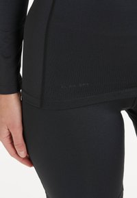 Schwarzes Sportoberteil mit langen Ärmeln, nahtlosem Design und figurbetontem Schnitt. Glatte Textur mit dezentem Markendetail.