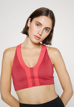 Sutien desportivo vermelho com um design em V, apresentando riscas cor-de-rosa contrastantes. Feito de um material ajustado e elástico. Comprimento curto com alças largas.