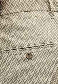 Κοντινή λήψη σε μπεζ και άσπρο καρό υφασμάτινο παντελόνι με πίσω τσέπη, κλειστό με κουμπί και ζώνη μέσης με θηλιές για ζώνη ορατές.